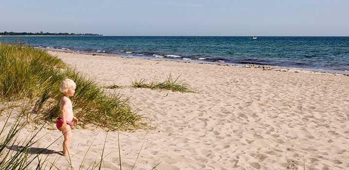 Ein kleines Kind steht in den Dünen und schaut über den Strand und das blaue Wasser hinaus