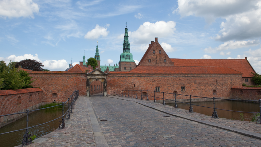 Schloss Frederiksborg in Hilleröd mit Backsteinportal über dem Schlossgraben, Kopfsteinpflasterbrücke und grünen Kupfertürmen